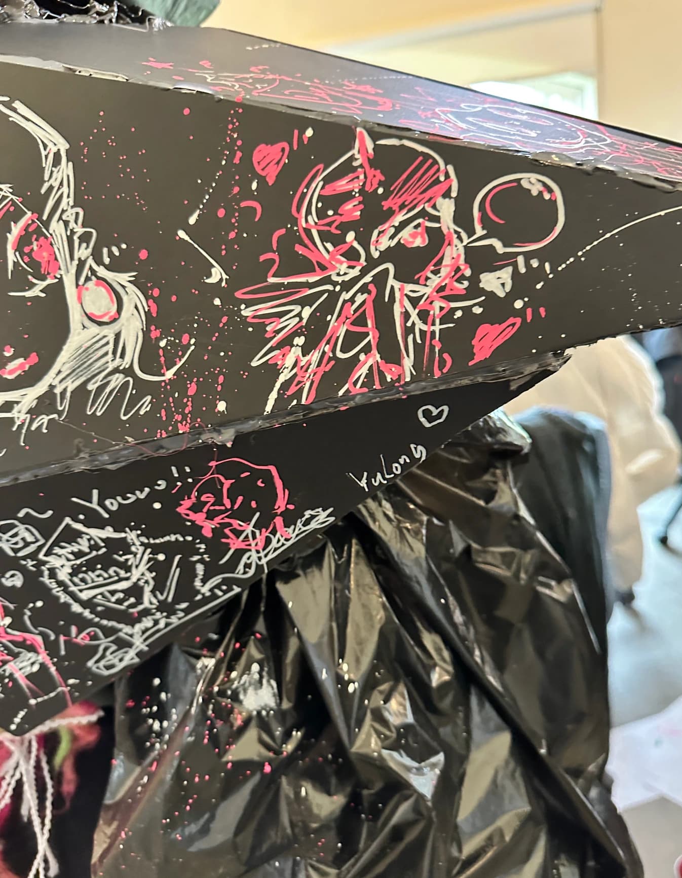 Black sculptural surface covered with white and pink drawings.