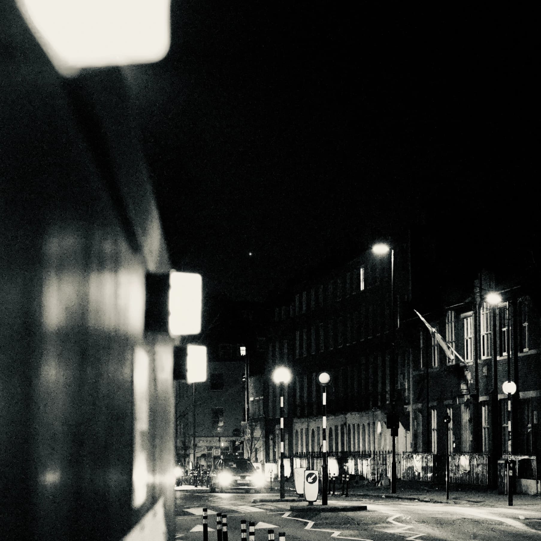 Black-and-white night street with lights reflected in a window.