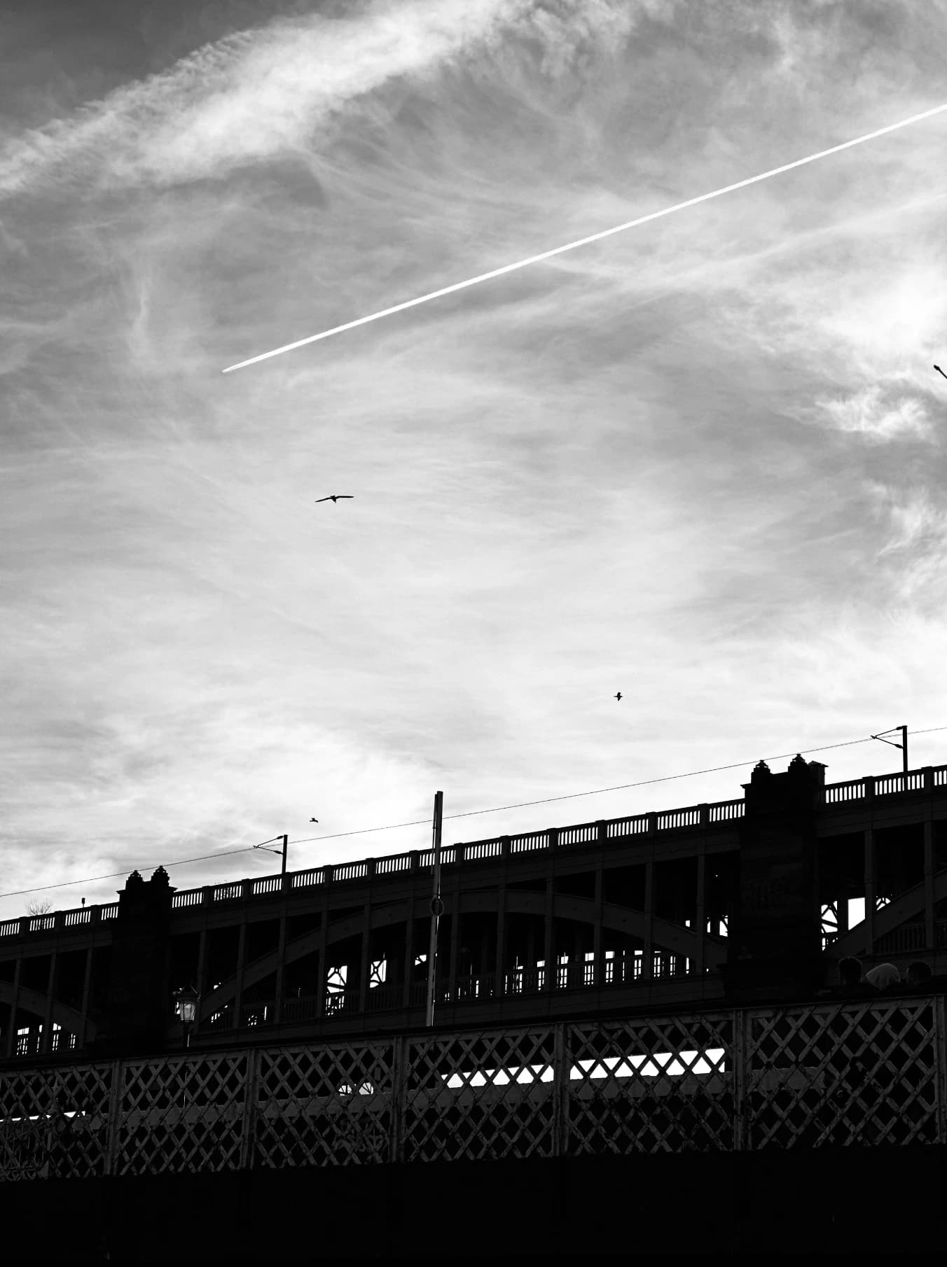 Sky and cloud trails above a bridge in black and white.